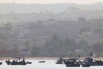 Kleine Fischerboote auf dem Wasser mit Palmen und Häusern an Land im Hintergrund.