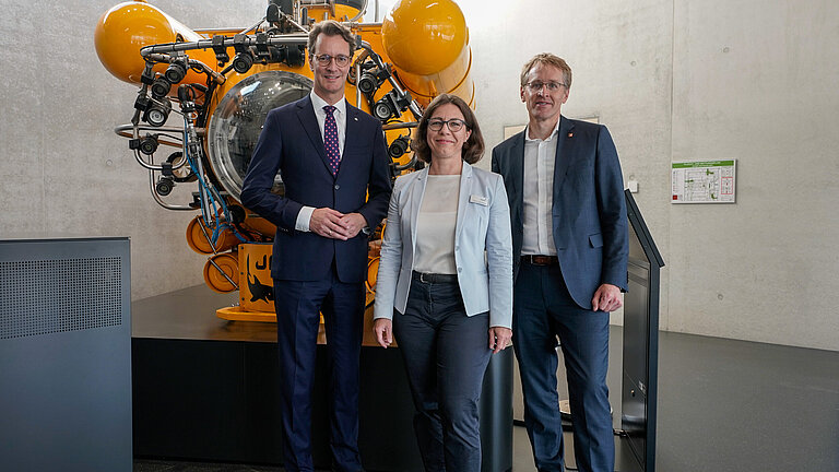 A woman and two men stand in front of a yellow underwater boat