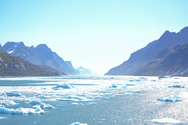 Eisschollen auf blauem Wasser in einem Fjord. Berge im Hintergrund. 