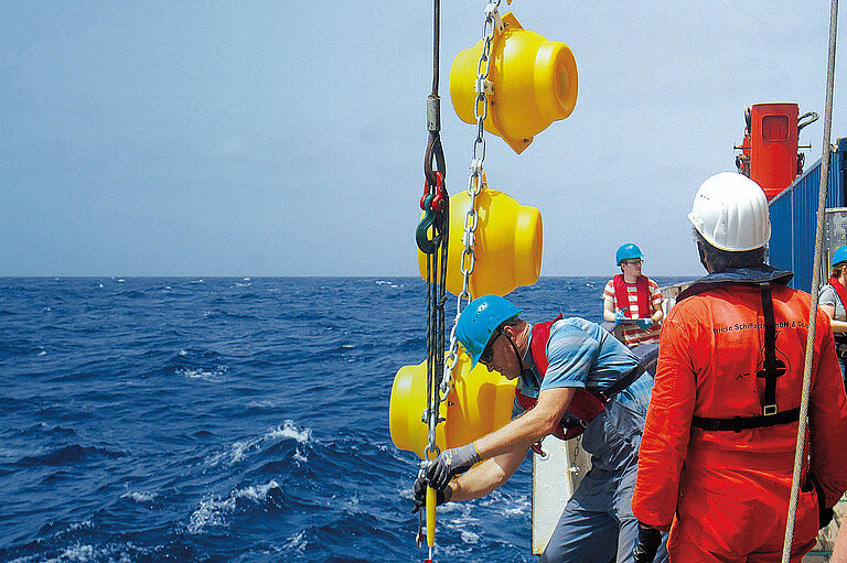 Two employees on a research vessel release a chain of large yellow balls into the water