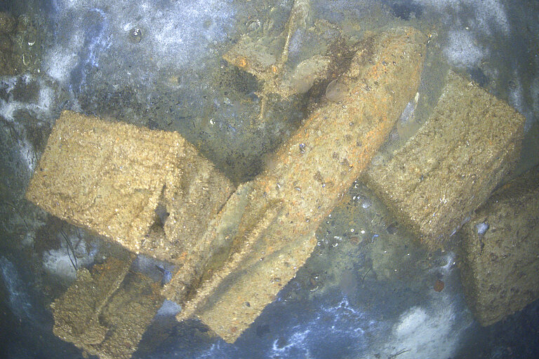 A torpedo and boxes of ammunition lie on the seabed