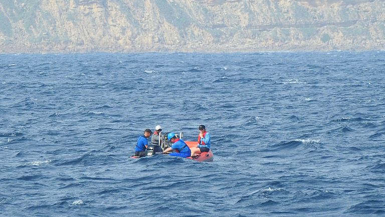 Ein kleines Schlauchboot mit vier Personen auf dem Meer, im Hintergrund ist die Küste zu sehen.