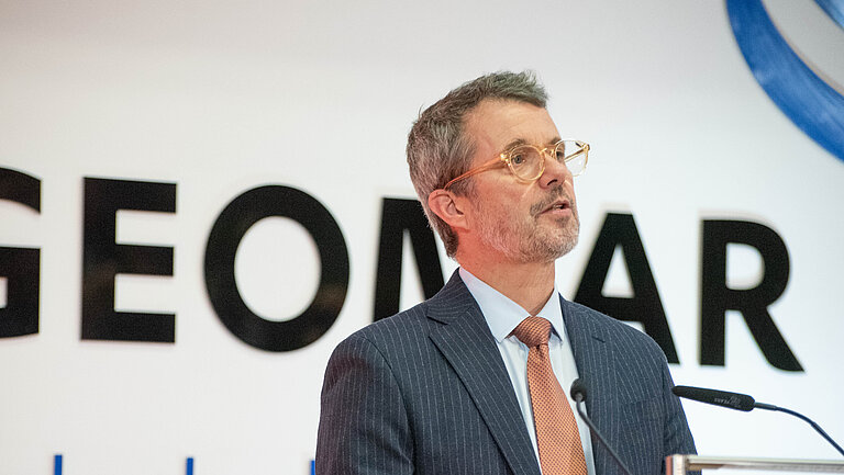 A man with glasses speaks in front of a wall on which the name ‘GEOMAR’ is written