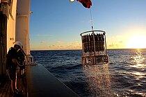 Ein Kranzwasserschöpfer wird bei Sonnenuntergang an Bord eines Forschungsschiffes gehievt