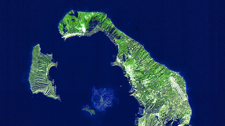 A satellite image shows a dark blue sea with ring-shaped green islands around a light blue shadow in the centre