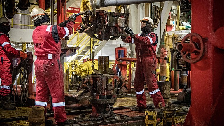 Men in red work suits remove a pipe from a yellow lift on board a ship