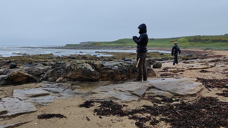 Person steht an der Küste auf Karbonsteinen in Schottland