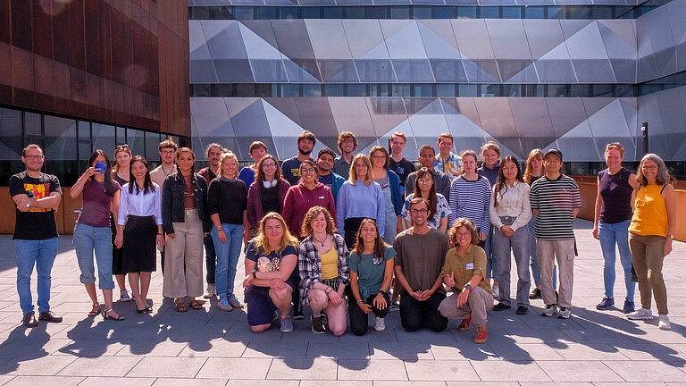 Eine Gruppe junger Leute posiert auf der Dachterrasse eines modernen Gebäudes für ein Gruppenbild.