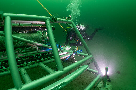 A metal frame is under water, a diver swims next to itprivate