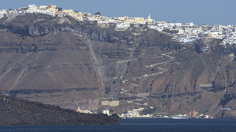 A rock face rises high out of the sea, with white houses on top